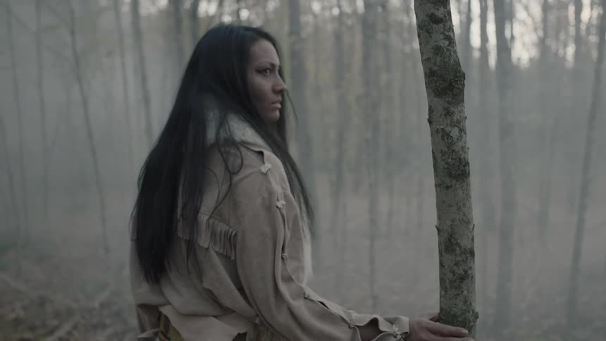 A woman stands among trees surrounded by haze