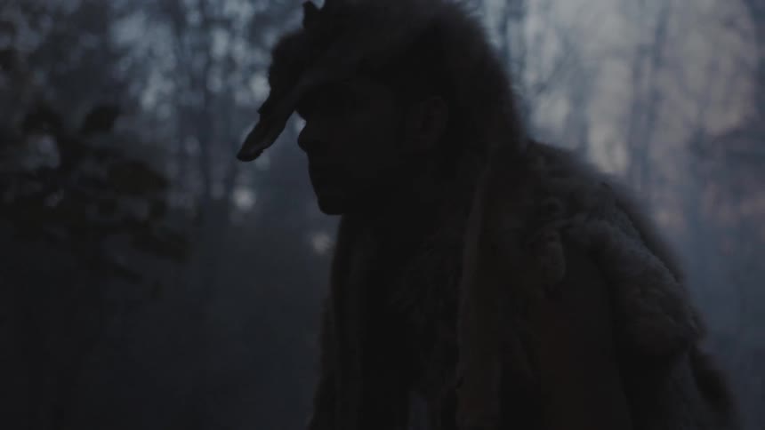 Man wearing a fox pelt over his head in a wooded area