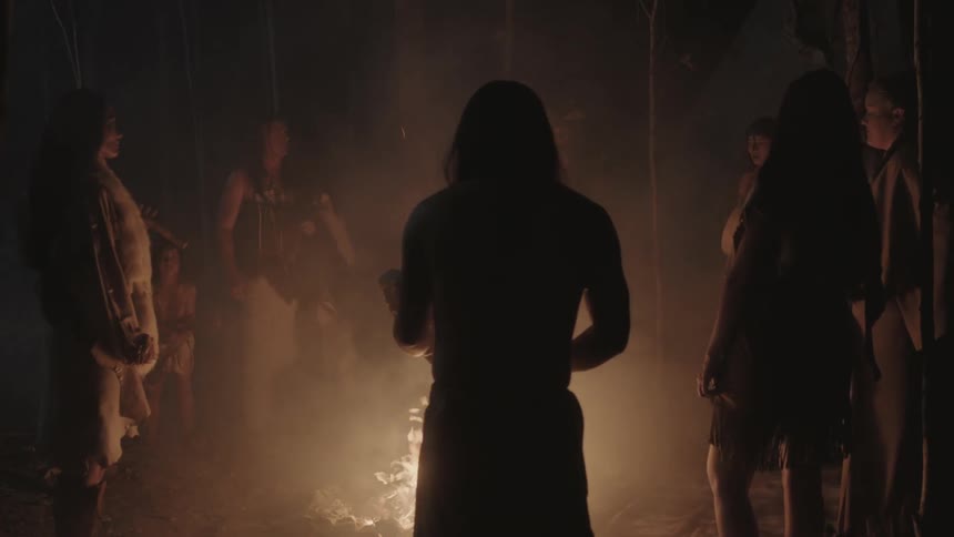 Tribe of people standing around a campfire at night