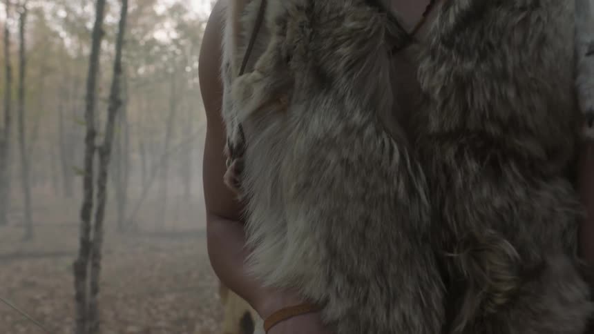 A native american man stands holding his bow and arrow ready