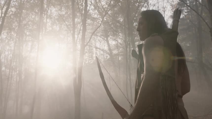 Native american man stands holding a bow in the sunlight