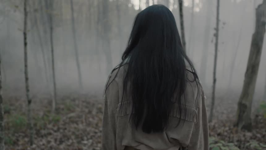 Long-haired woman walking slowly through a smoky forest