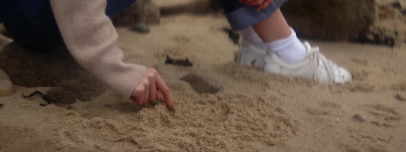 Child sitting over a rock draws on the sand with a finger