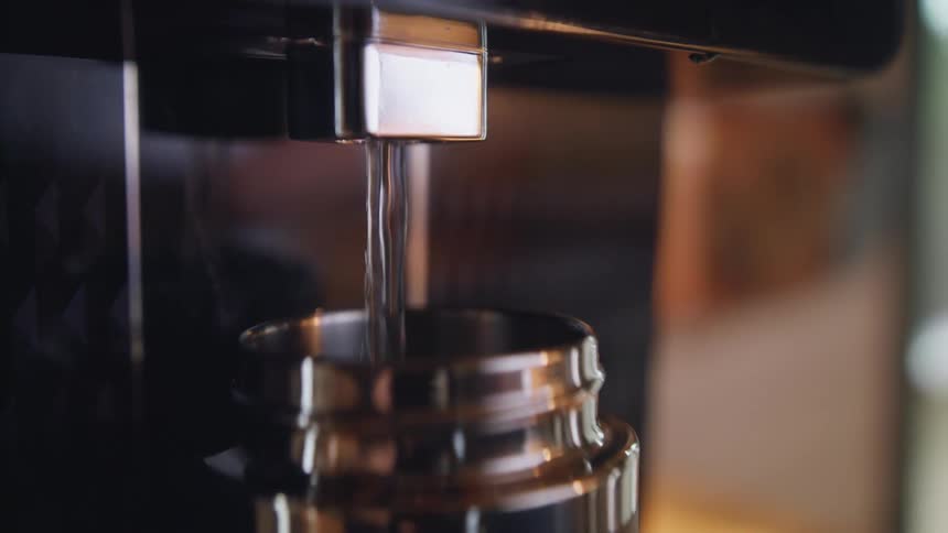 Close up of hot water is being poured into aluminum bottle from espresso machine