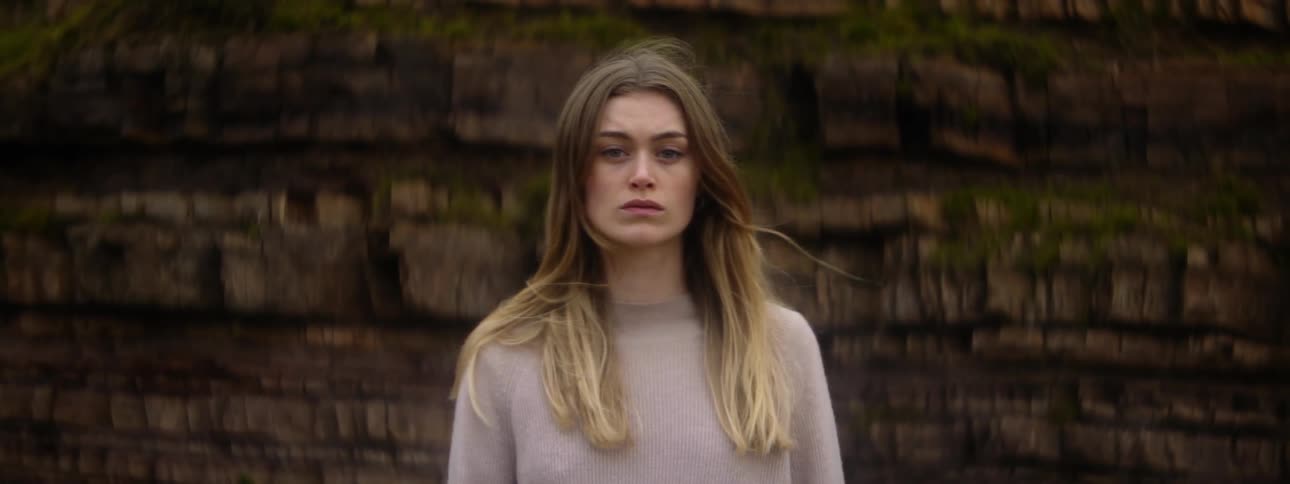 A woman is standing outside near a wall as her hair moves in the breeze
