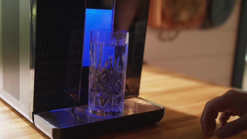 A man gets a glass of water from an electronic dispenser at home