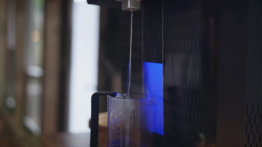 Water coming out of a spout on a coffee machine in to a glass of coffee