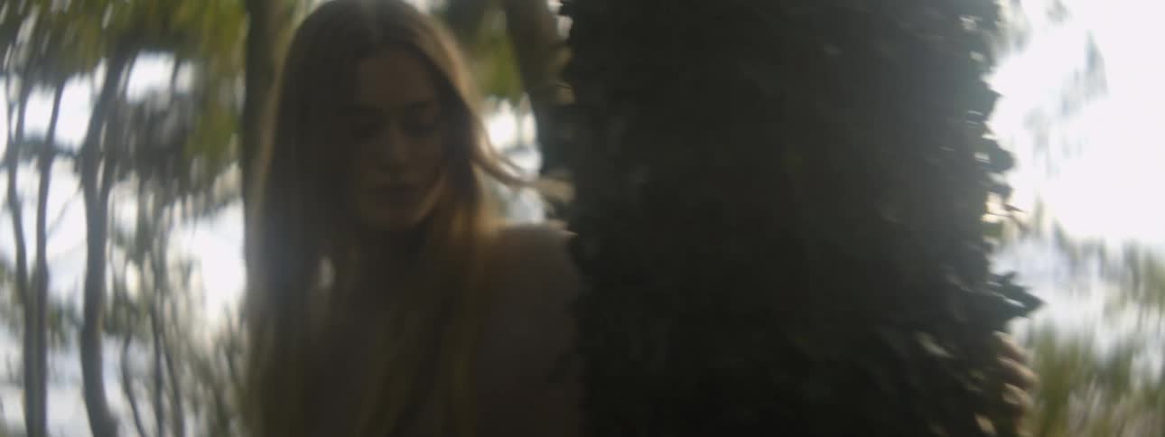 Blonde woman wearing brown sweater touches tree trunk in the woods