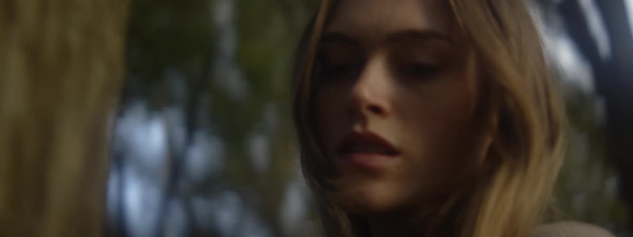 Close up of the face of a woman walking around a tree while touching the trunk with her hand