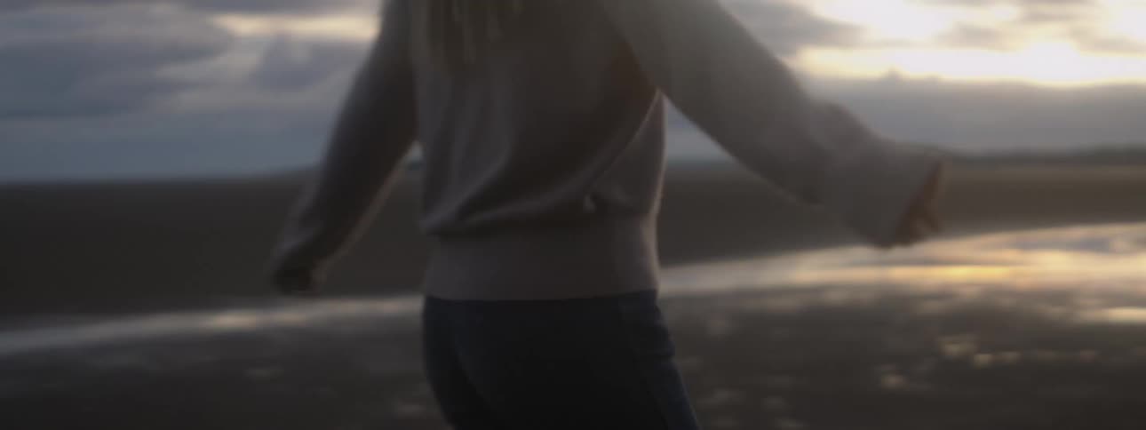 A woman spins in circles on a beach as the sun sets