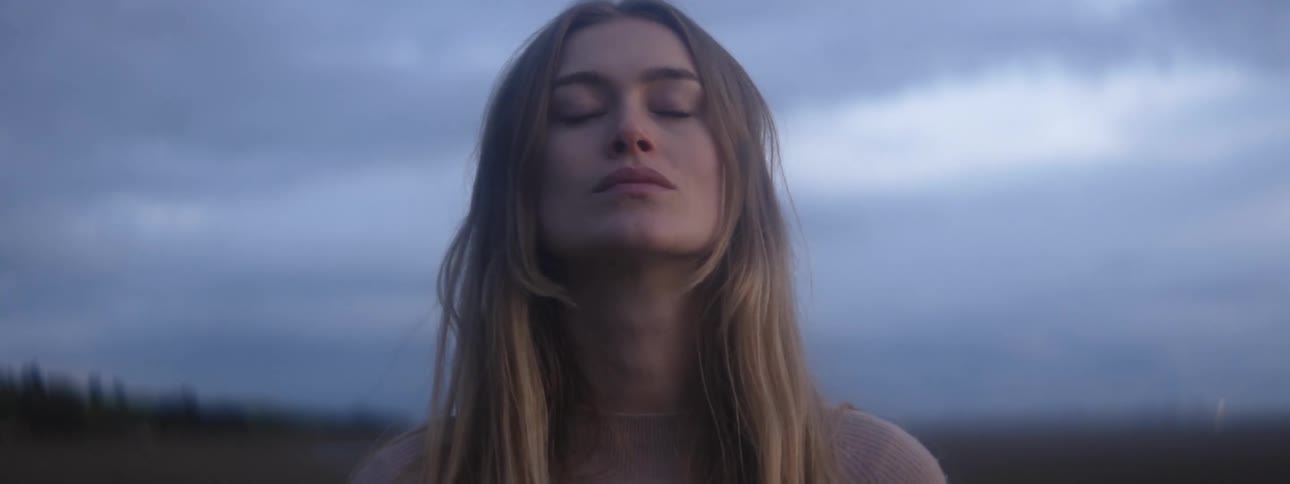 A woman is standing outside under a cloudy sky and she closes her eyes
