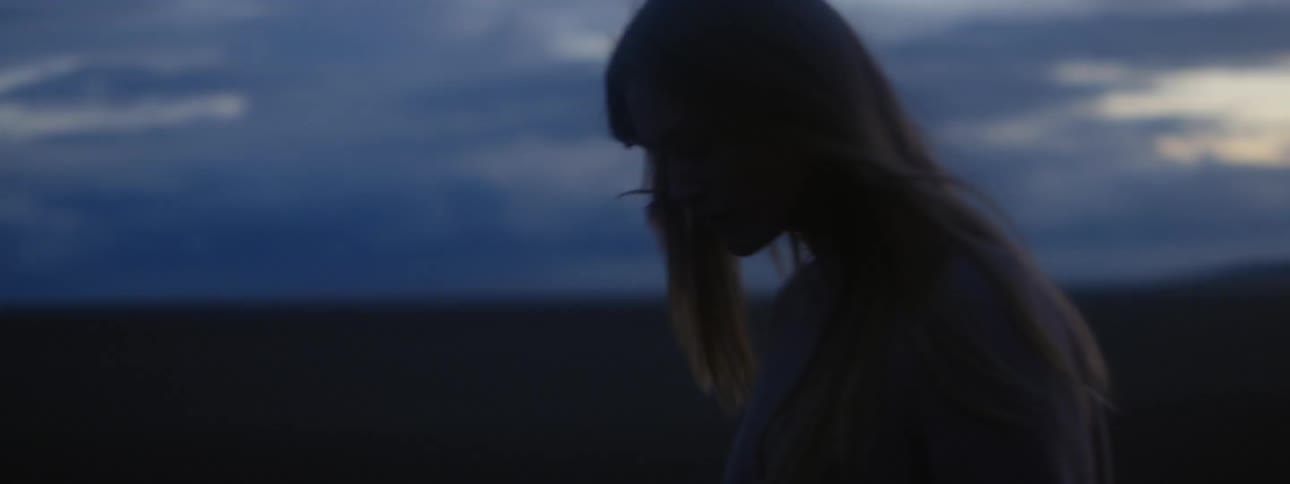 Young blonde woman with long hair walking through a rural field at evening