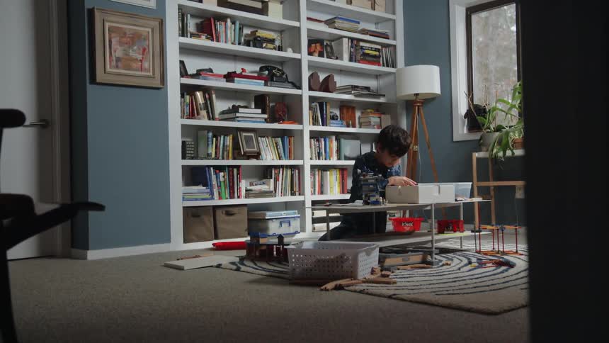 A child kneels at a small table while sorting through a box of toys