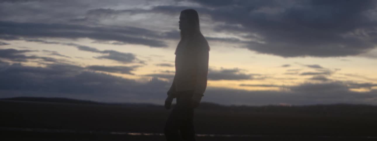 Woman walks under red tinted sky with hills in the background