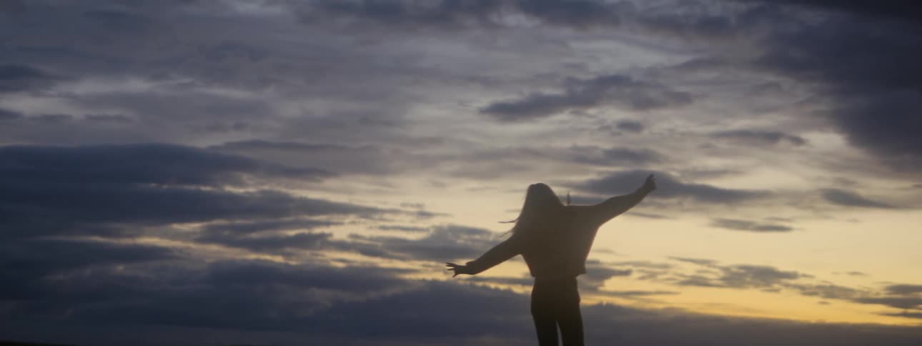 Silhouette of a young woman spinning around a field in the countryside at evening