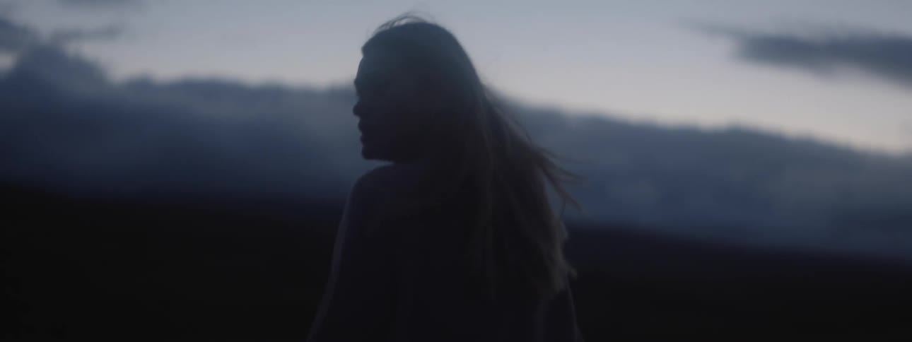 Blonde woman walking in the field is silhouetted against the sky at dusk