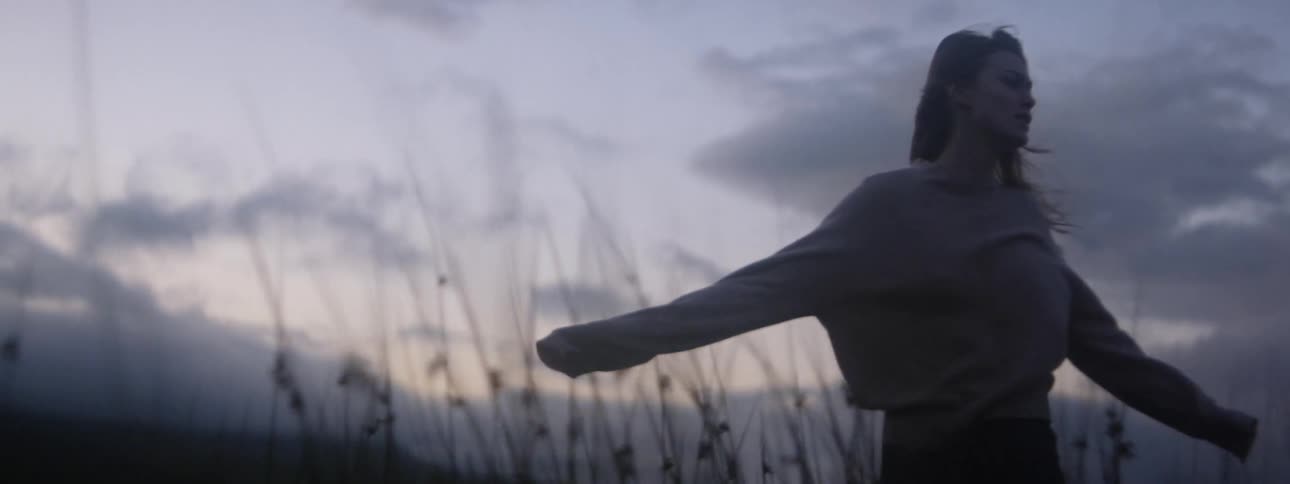 A young woman walking through tall grass in a field at sunset