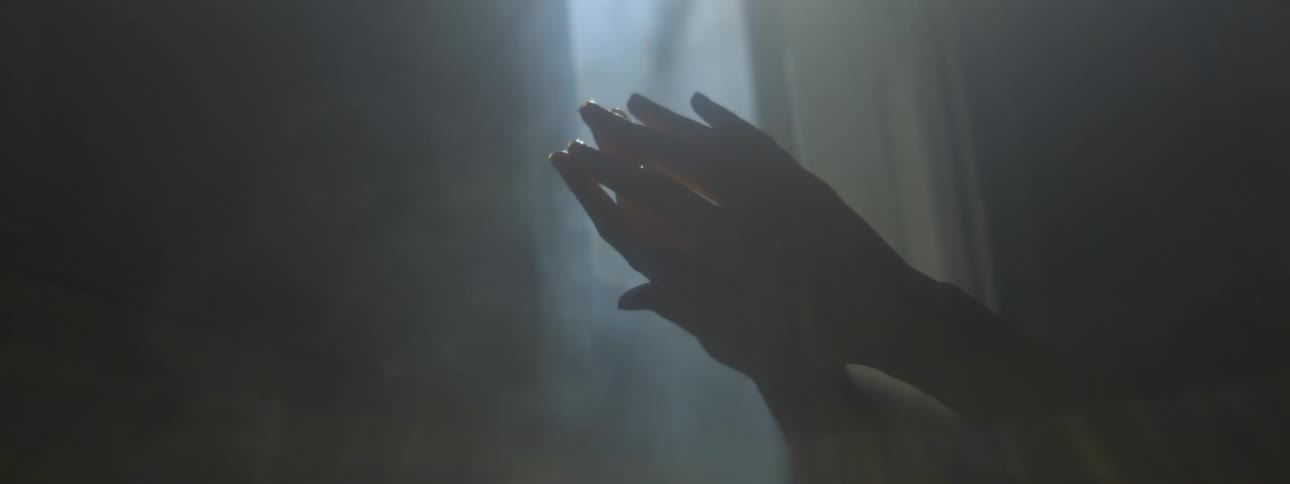 Close up of womans hands are silhouetted against the light in foggy dark room