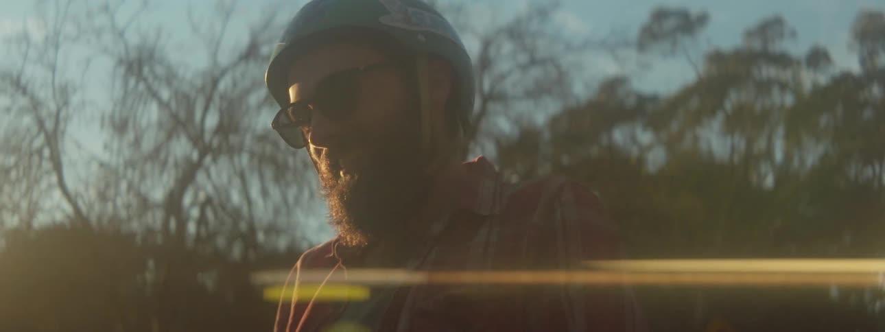 Male skateboarder with beard sunglasses turquoise helmet and red shirt in the countryside