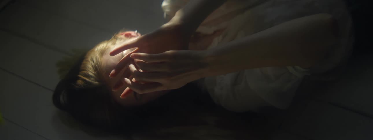 Blonde woman wearing white shirt lies on floor touching her hands