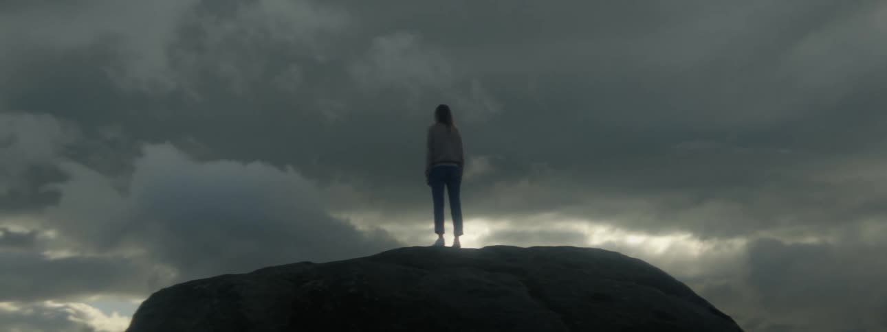 Woman standing on big rock against the cloudy sky