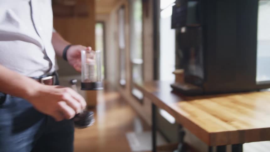 A man at home puts a glass cannister under a spout on a coffee machine as he prepares coffee