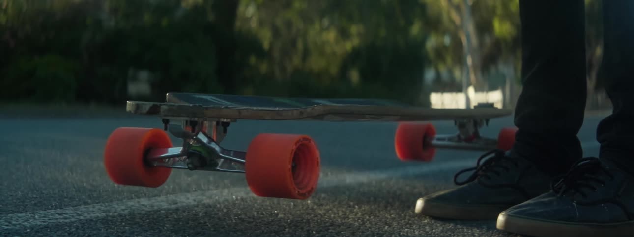 A skateboard falls onto the pavement and bounces near someones feet