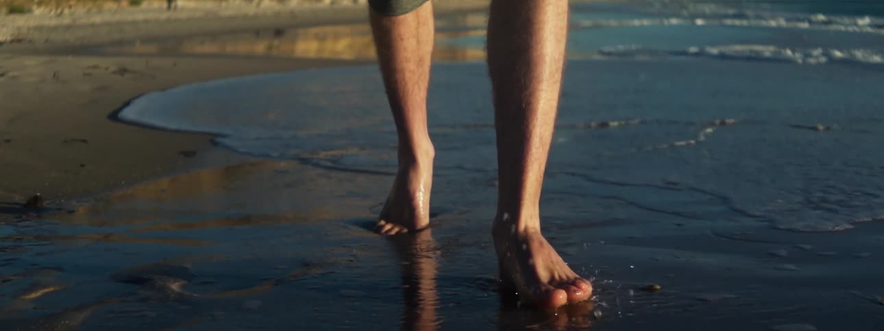 Barefoot man with rolled up pants walks through wet sand on beach