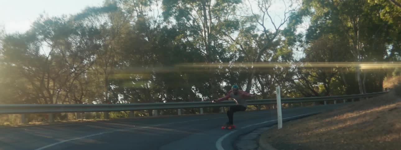 A skateboard rider is squatting down as they go around a curve and the sun is shining brightly in the distance