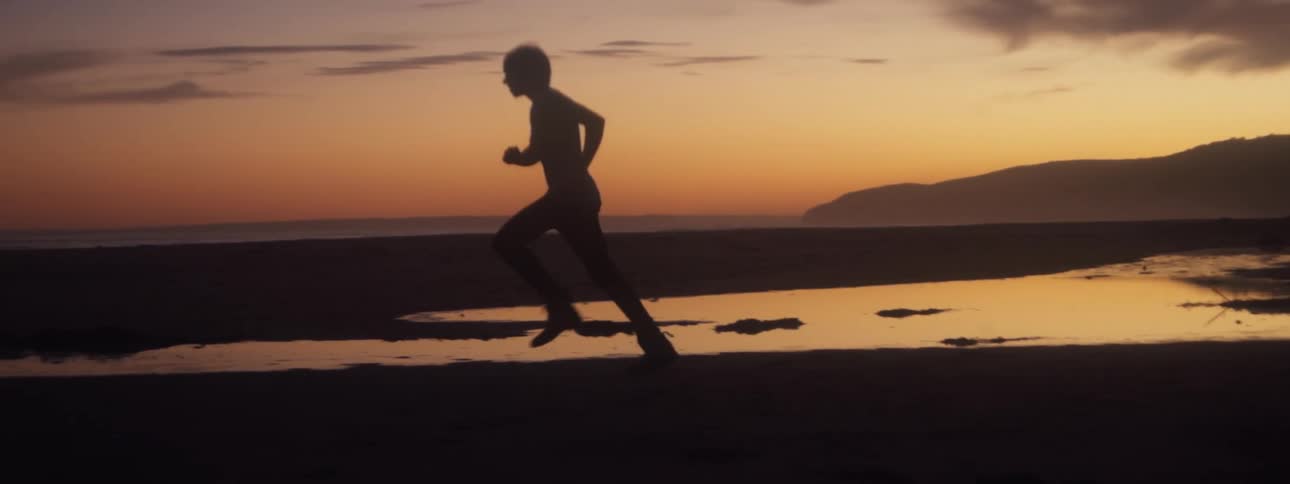 The silhouette of a young man running at the beach against a golden sky