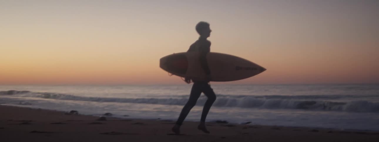 A man runs carrying a surf board runs towards the ocean