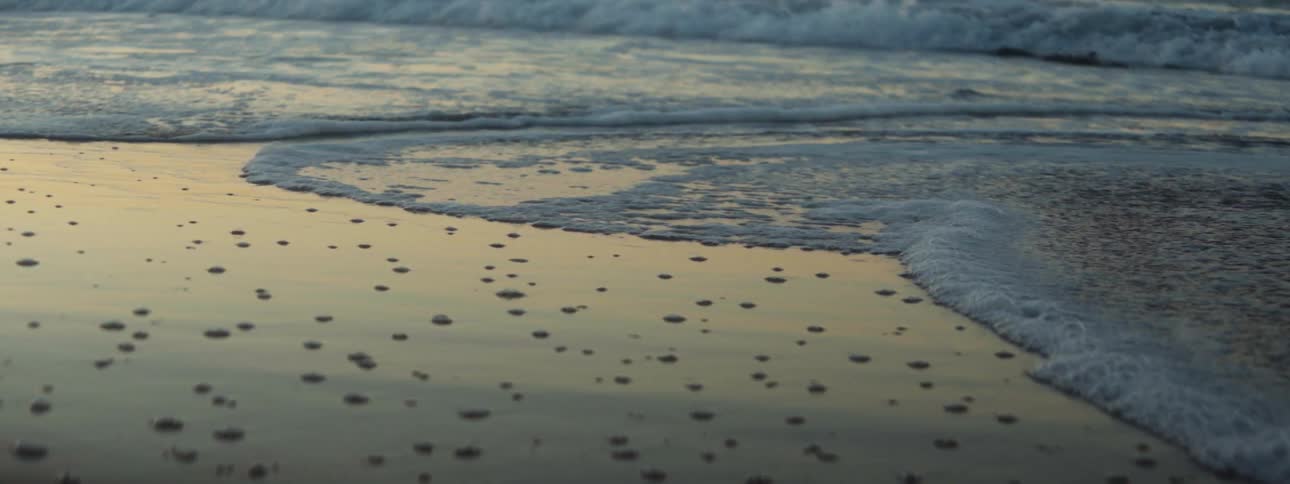 Surf crashes onto beach foaming over the sand under a red tinted sky