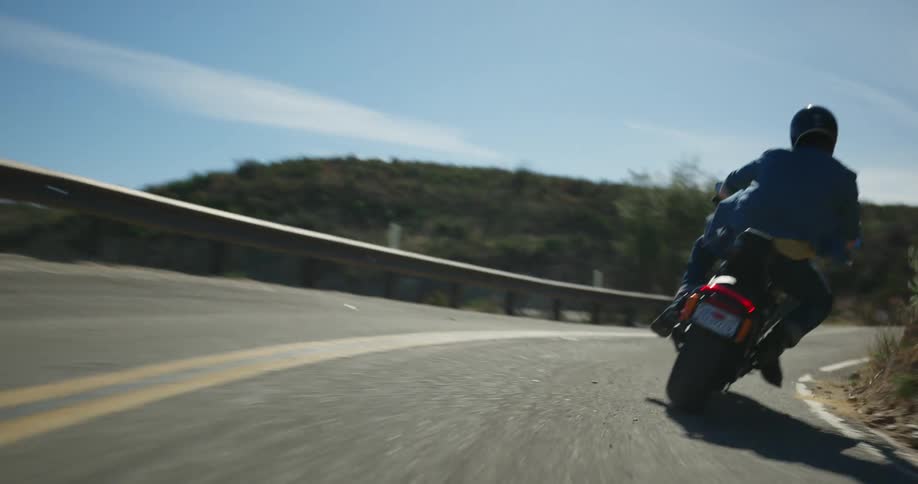 Man with helmet and blue shirt rides motorcycle up the mountain road