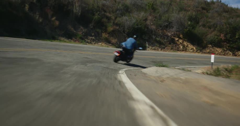 A motorcyclist drives very quickly around a turn in a winding road