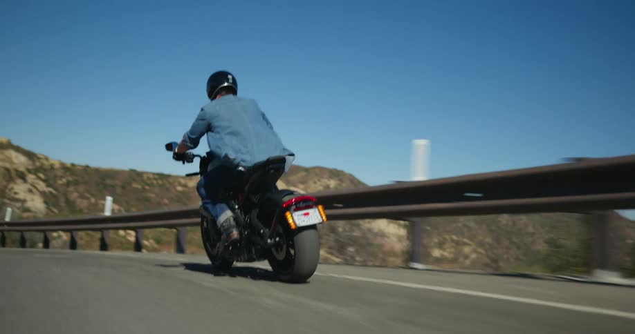 Man with black helmet blue shirt and jeans rides motorcycle on mountain highway