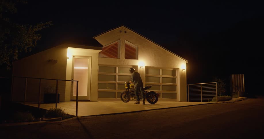 A man exits the house to climb on a motorcycle parked at the front at night