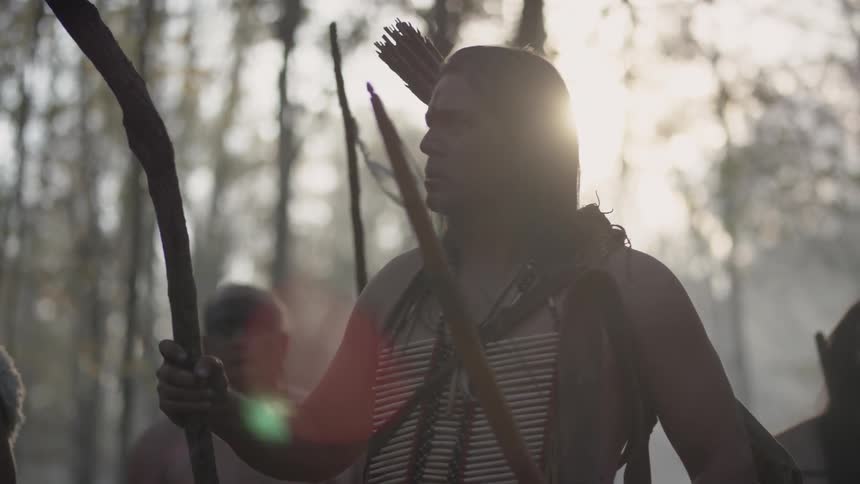 Tribal men standing around in a wooded area