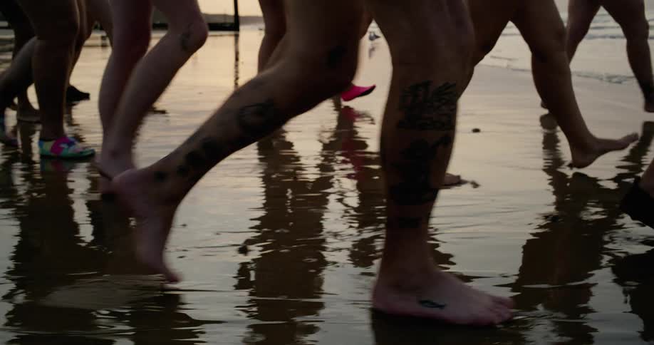 A group of swimmers walking toward the ocean waves together feet walking on wet sand then wading in water