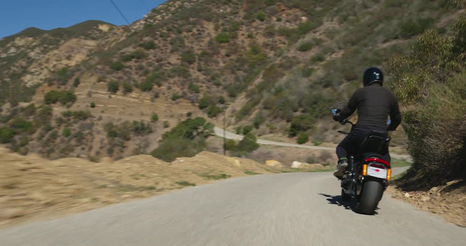 Motorcyclist rides motorcycle along highway past hills