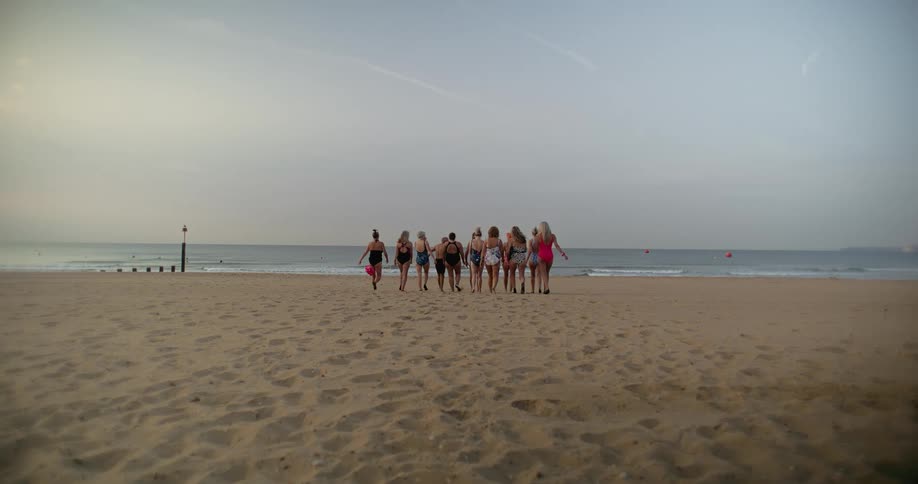 A group of friends in bathing suits walking toward the ocean waves