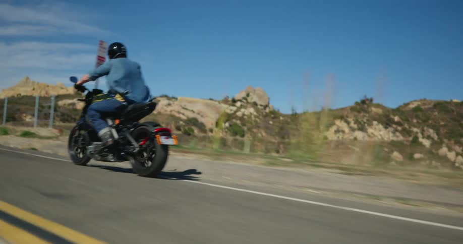 Male biker wearing helmet blue shirt and jeans rides motorcycle uphill in the mountains