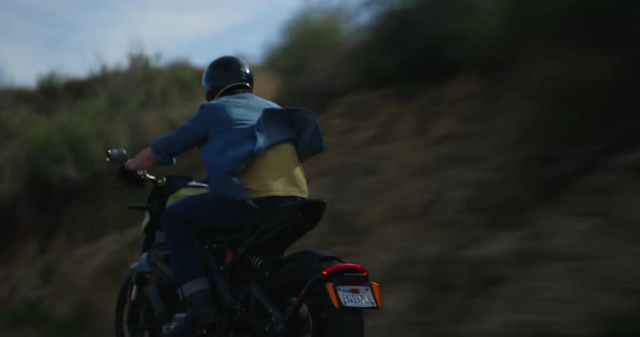 A man wearing denim apparel races along a road on his motorcycle