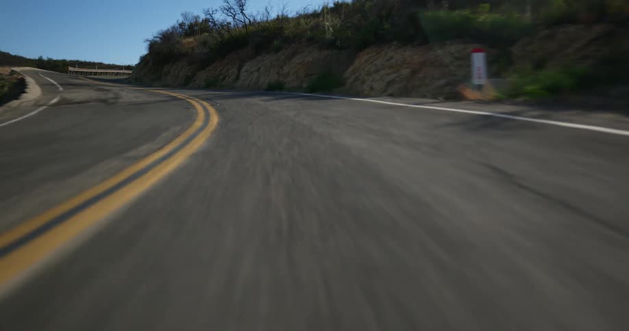 The camera moves fast down a road surrounded by trees as if it is in a vehicle but the vehicle is unseen
