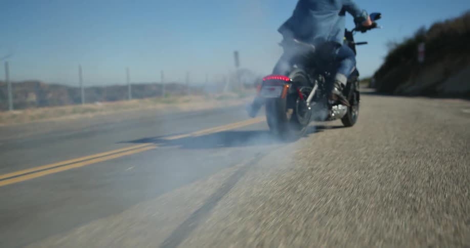 Man sitting on a motorcycle burns rubber and starts running on a road in the mountains