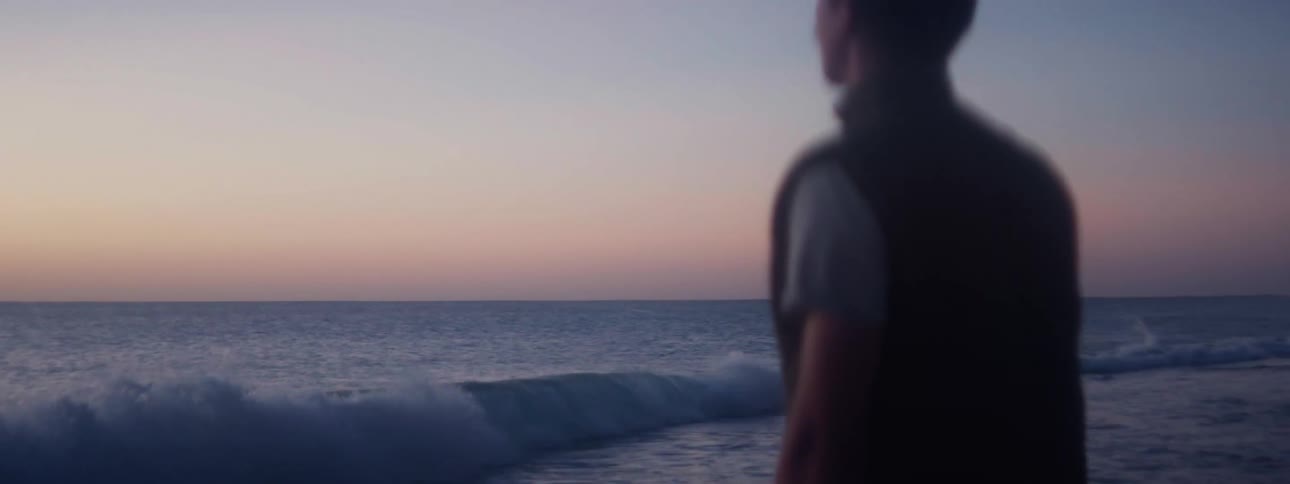 Man throwing a small rock into the sea in the empty beach at sunset