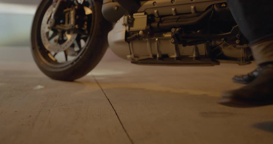 A person walks up to a parked motorcycle before they sit atop it and roll away