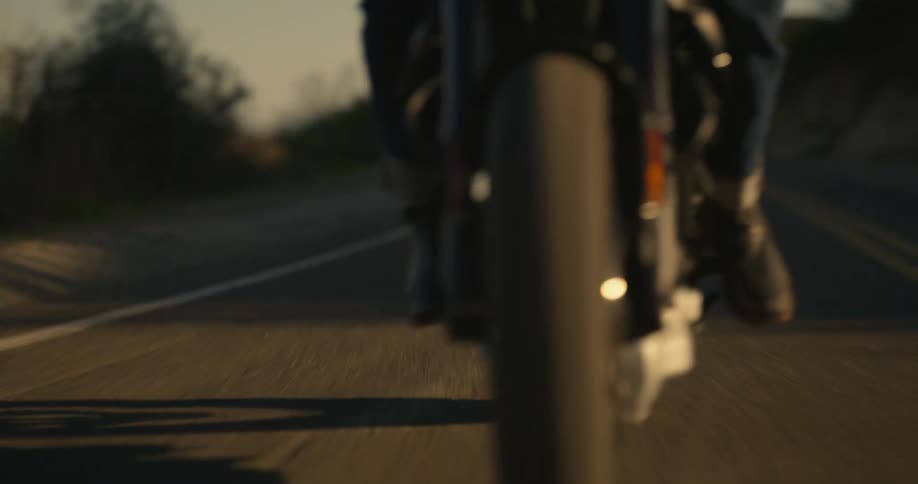 Man rides a motorcycle downhill on a road on the mountains at evening
