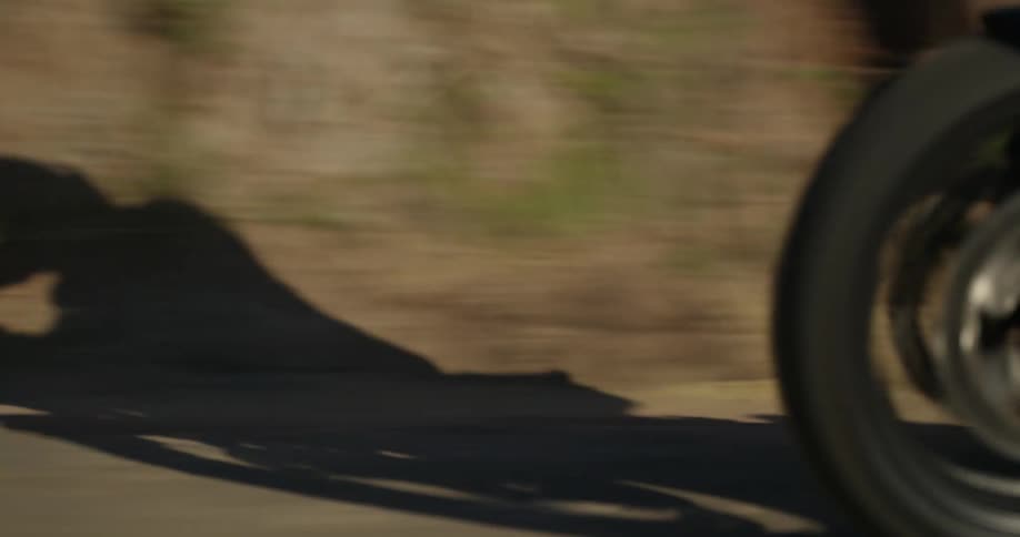 Shadow of a man riding a motorcycle downhill on a road on the mountains at daytime