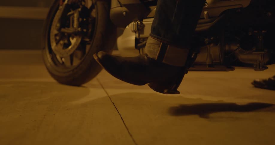 Man sitting on a motorcycle parked in a garage at night retracts the bike kickstand