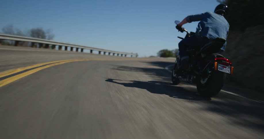 A person rides a motorcycle along a mountain road under a clear day